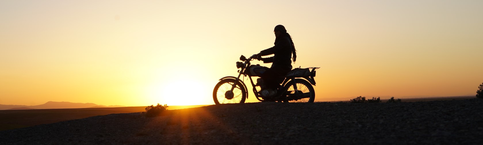 Silhouette of person on motorcycle at sunset, from Cutting Through Rocks