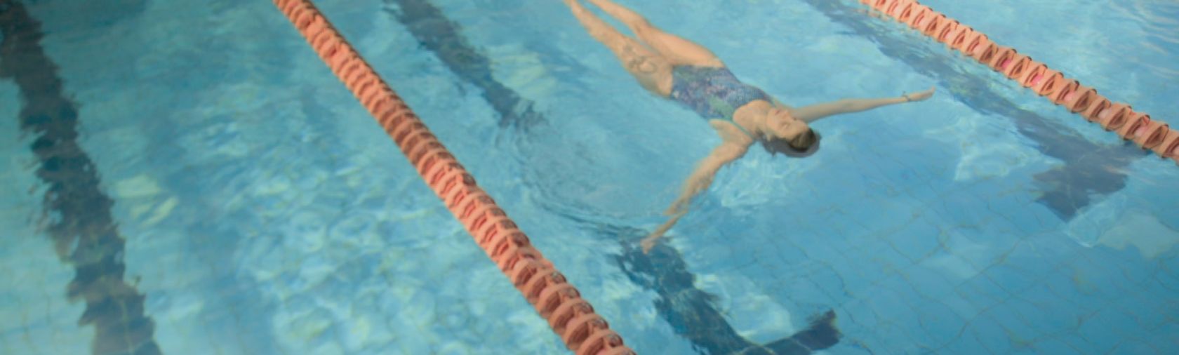 Woman in a blue one-piece bathing suit floats facing upwards in a pool