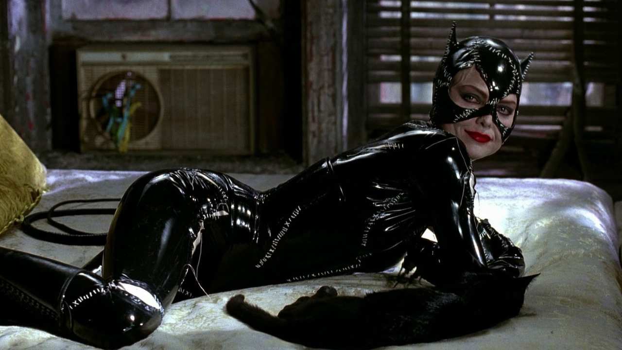 a woman in a black cat suit laying on a bed