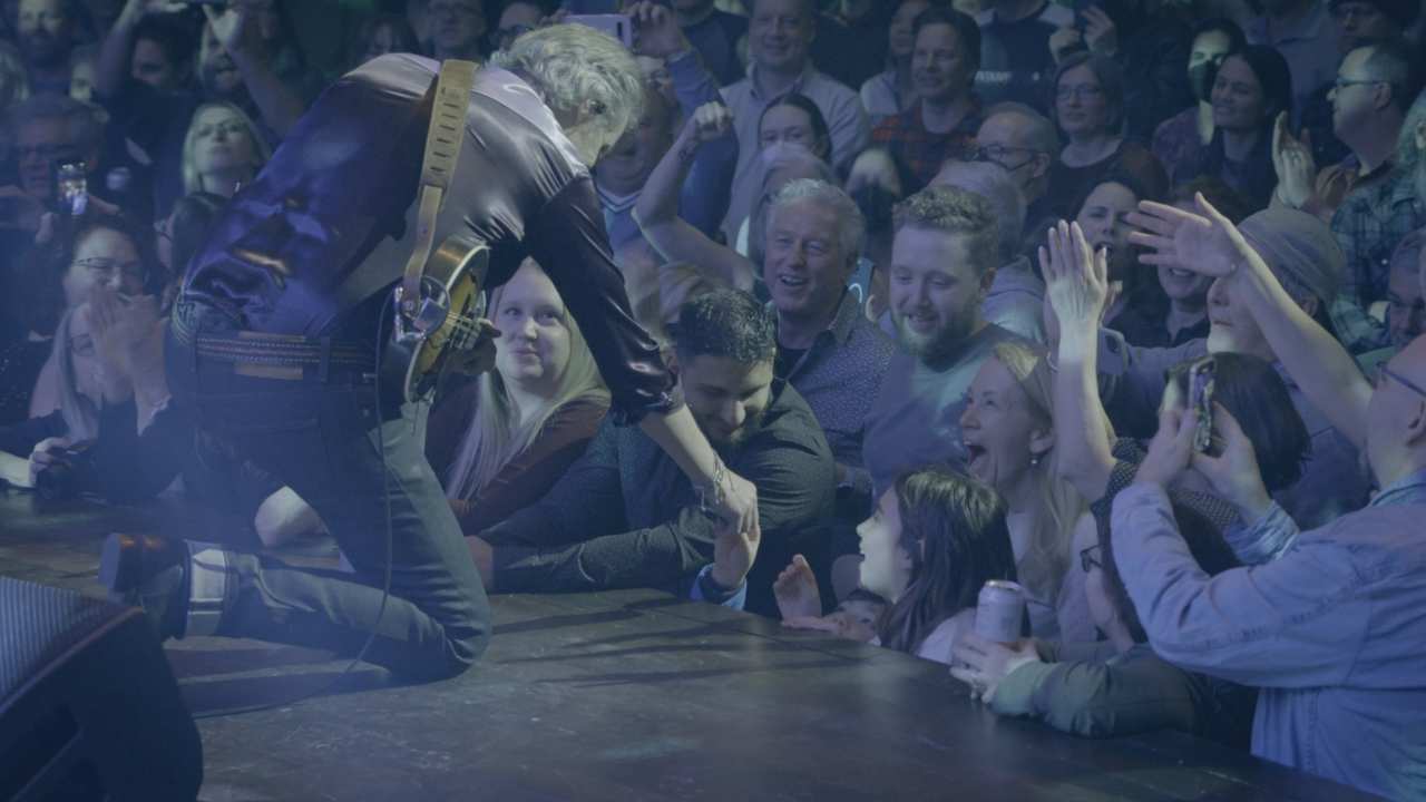 a man on stage with a guitar reaching out to a crowd of fans