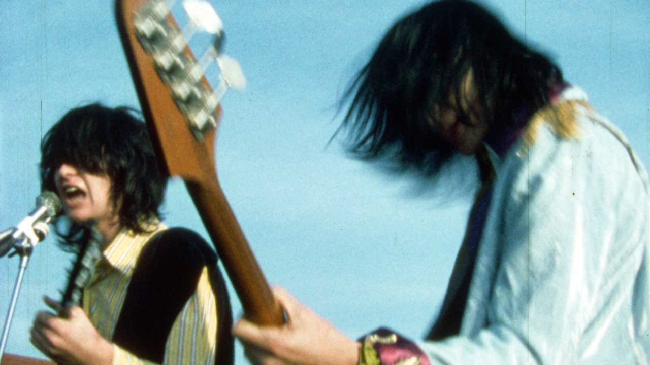 two people with long hair singing and playing guitar