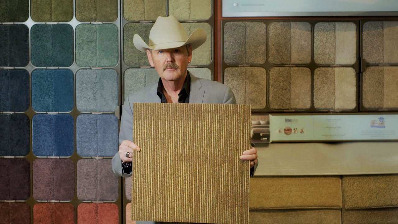 a man with a cowboy hat holding a square of carpet
