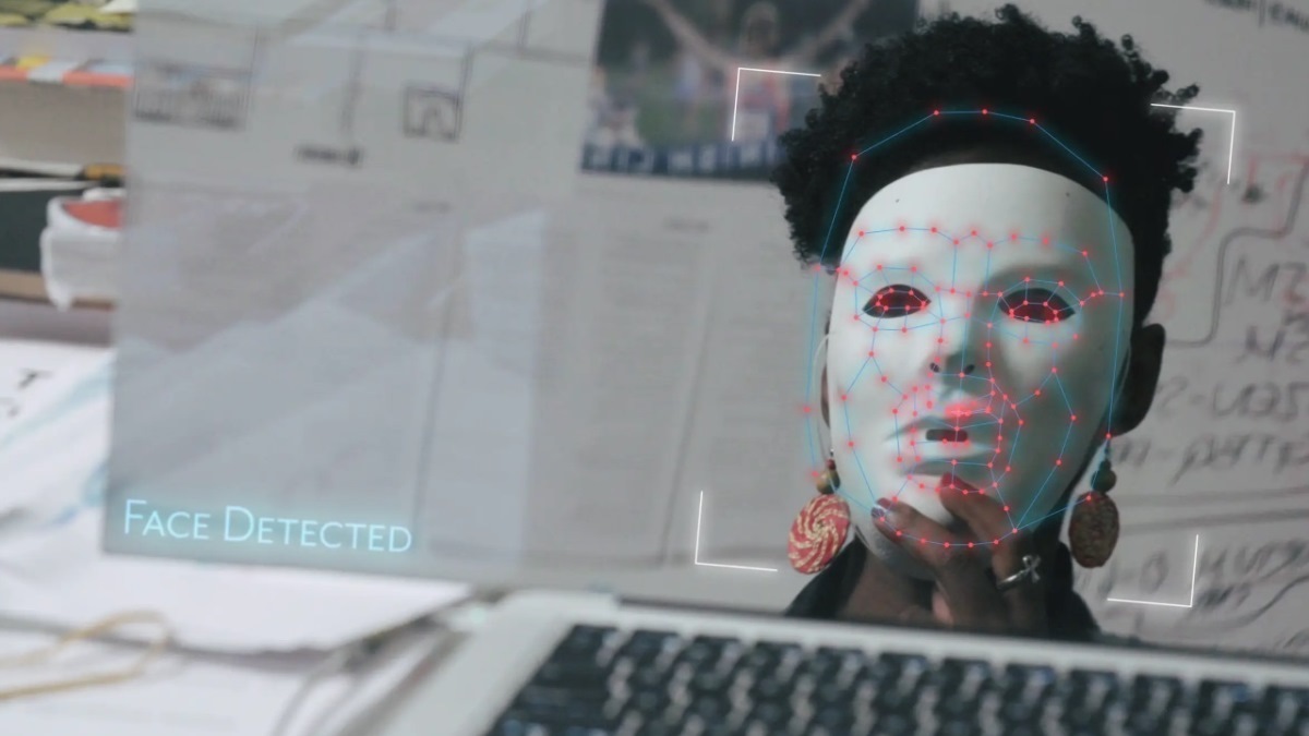 Black woman holding white mask to face being scanned