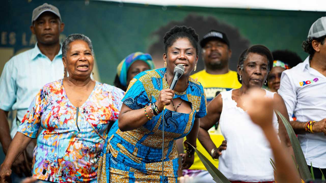 a woman speaking into a microphone in front of a group of people