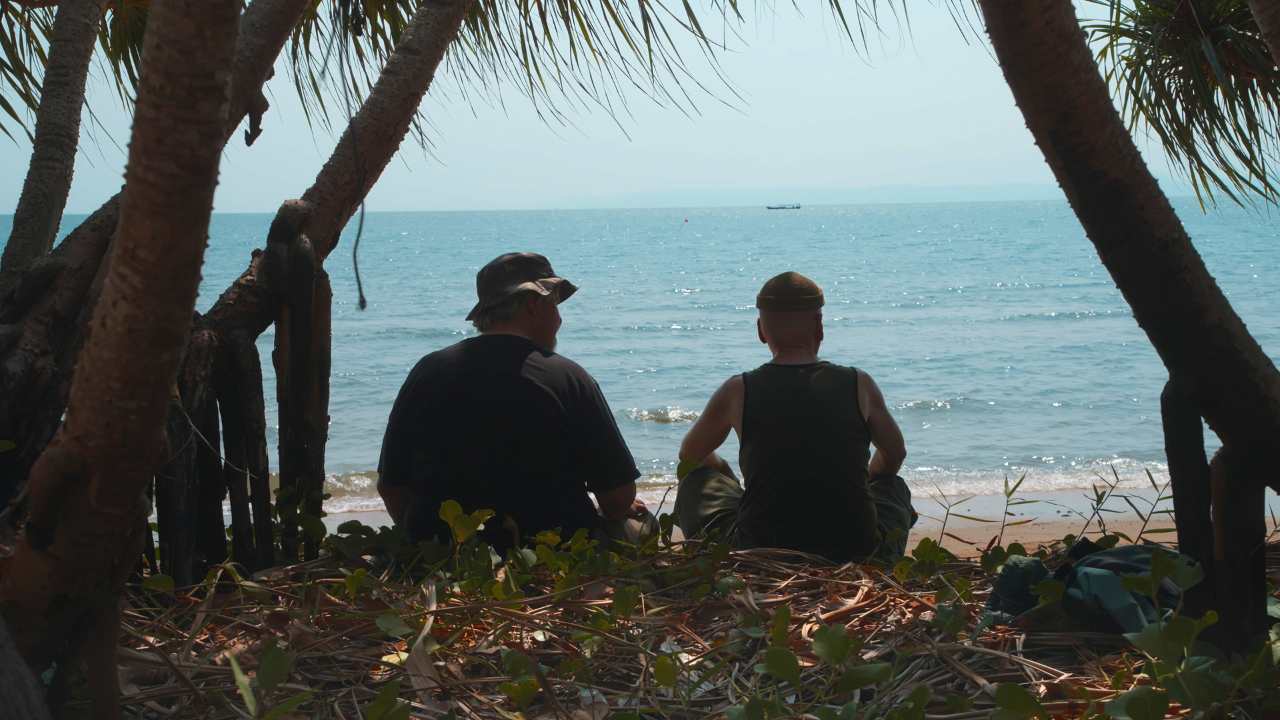 two men sitting together talking on a beach