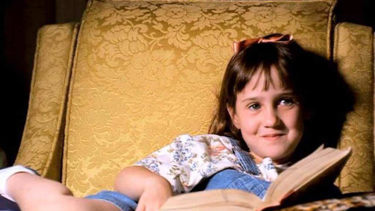 a little girl sitting on a chair with a book