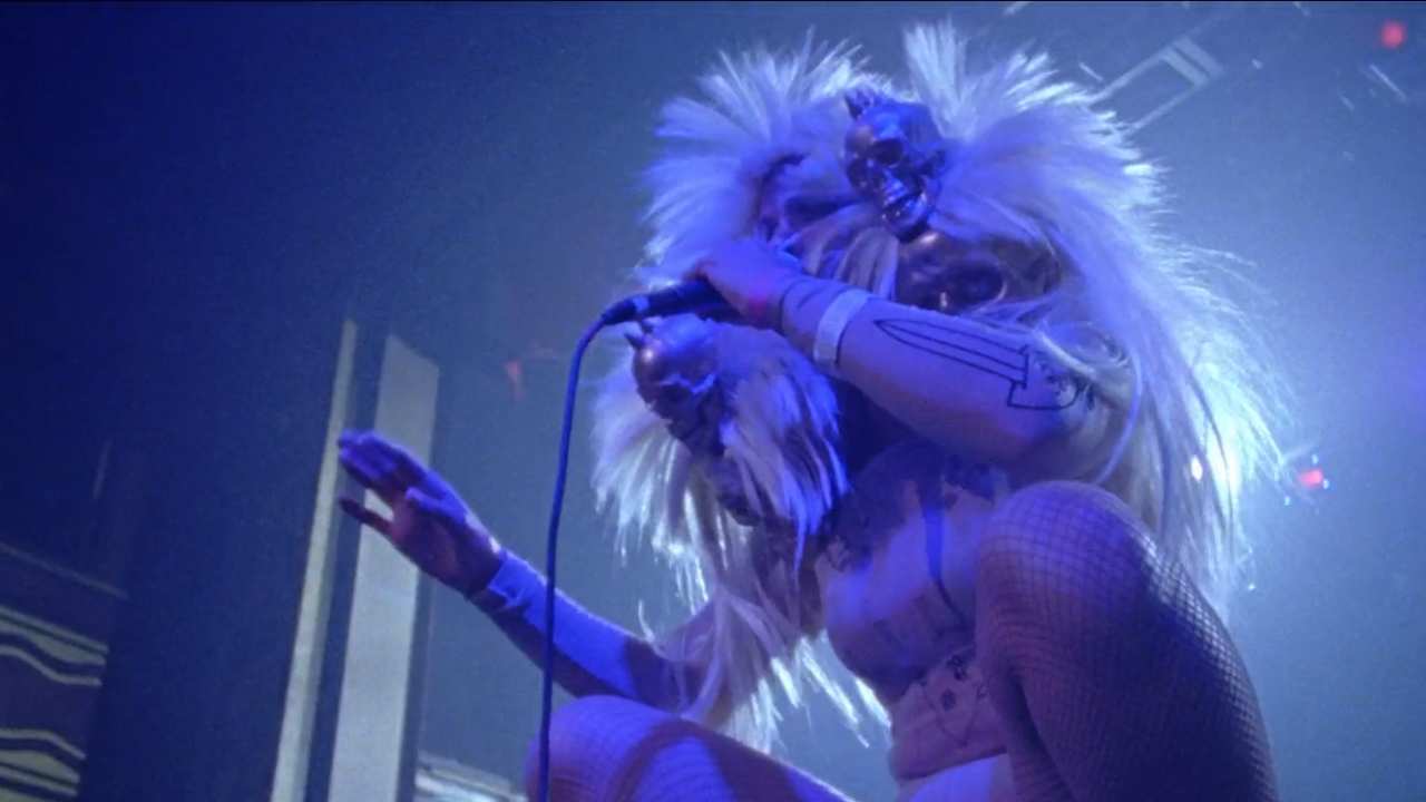 Peaches singing on stage in a coloured wig with skulls and fishnet tights