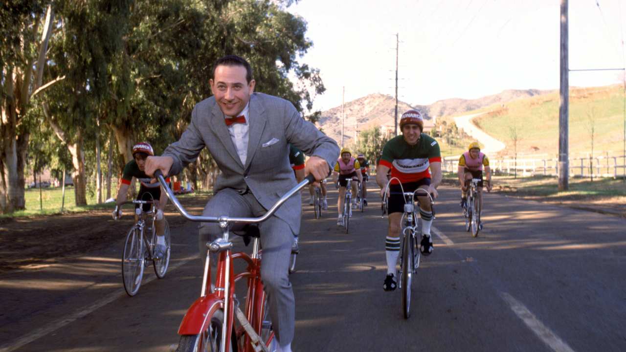a man in a gray suit and bowtie riding a bike