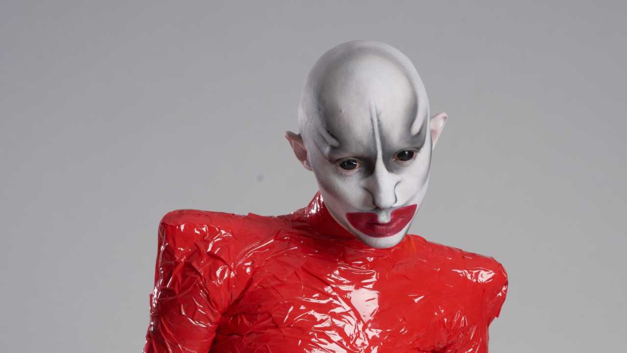 an artist with elaborate makeup and wearing a red PVC outfit