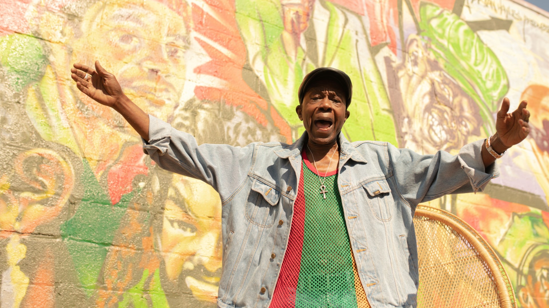 Black man with arms out, in front of graffiti