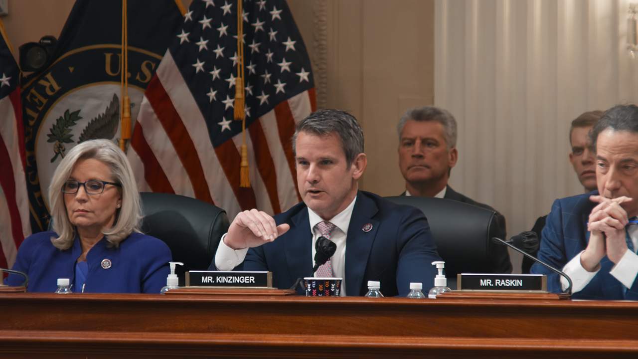 a group of people in business wear sitting at a long table in front of a USA flag