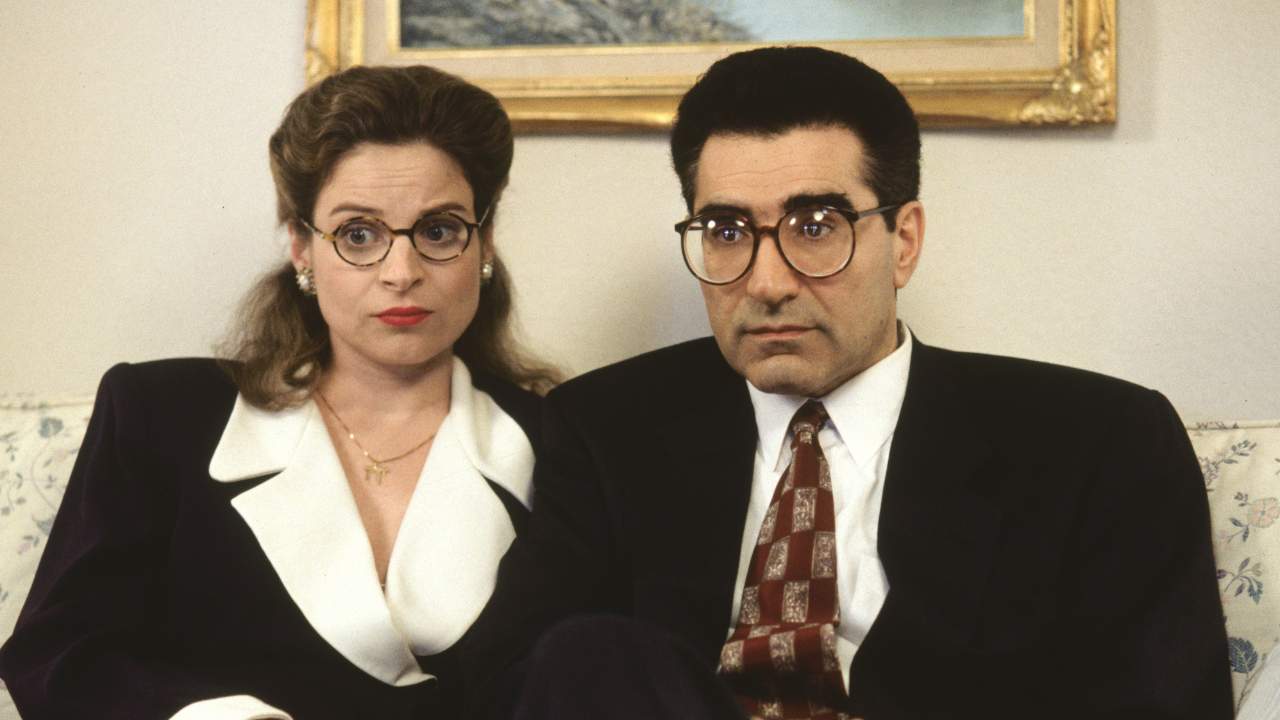 a woman and a man with glasses in suits sitting together