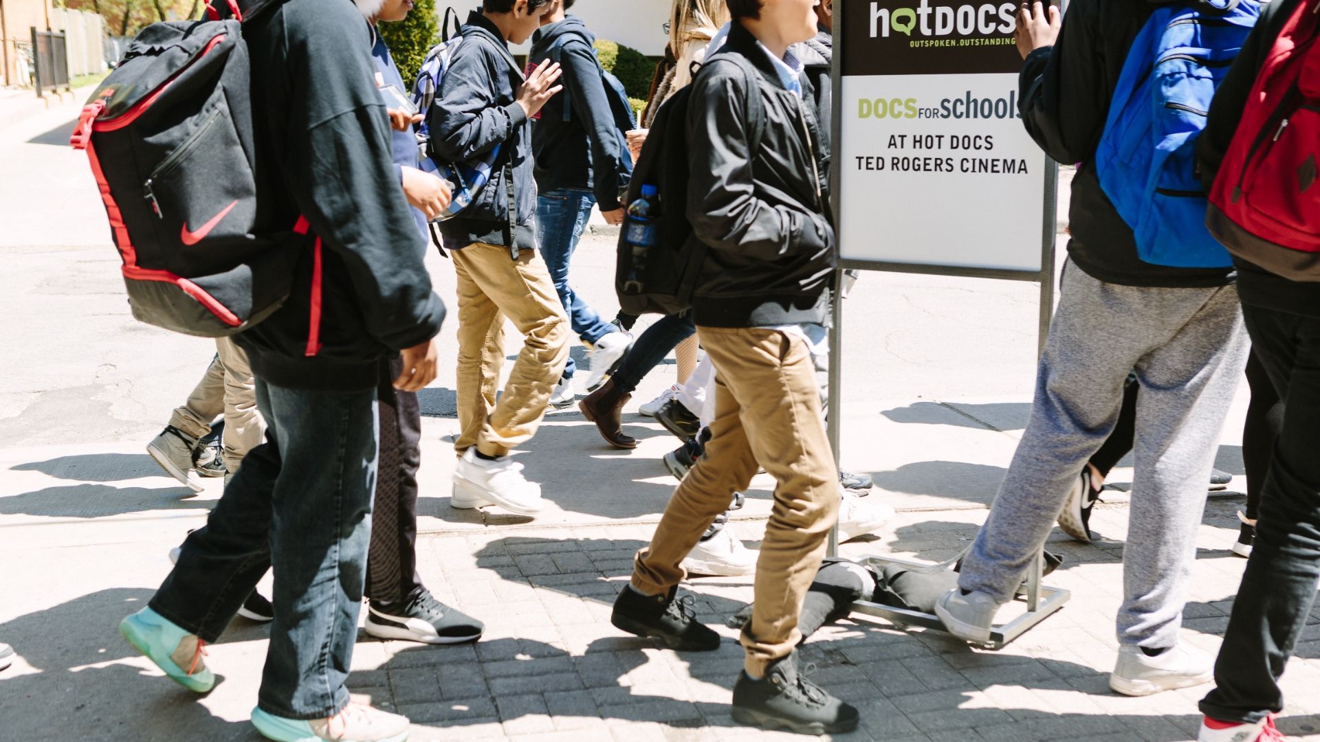 School age children in streetwear walking past a Docs for Schools outdoor sign.