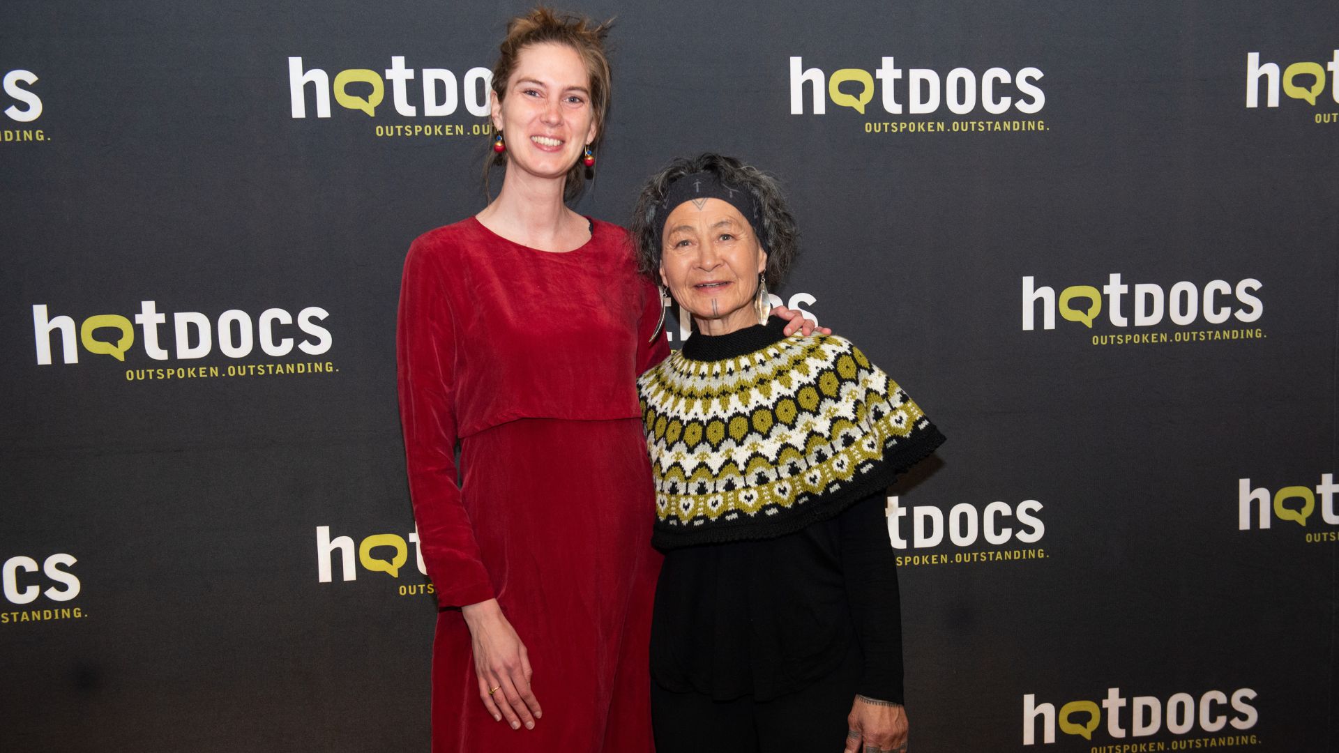 Director Lin Alluna and film subject Aaju Peter stand smiling in front of Hot Docs step and repeat