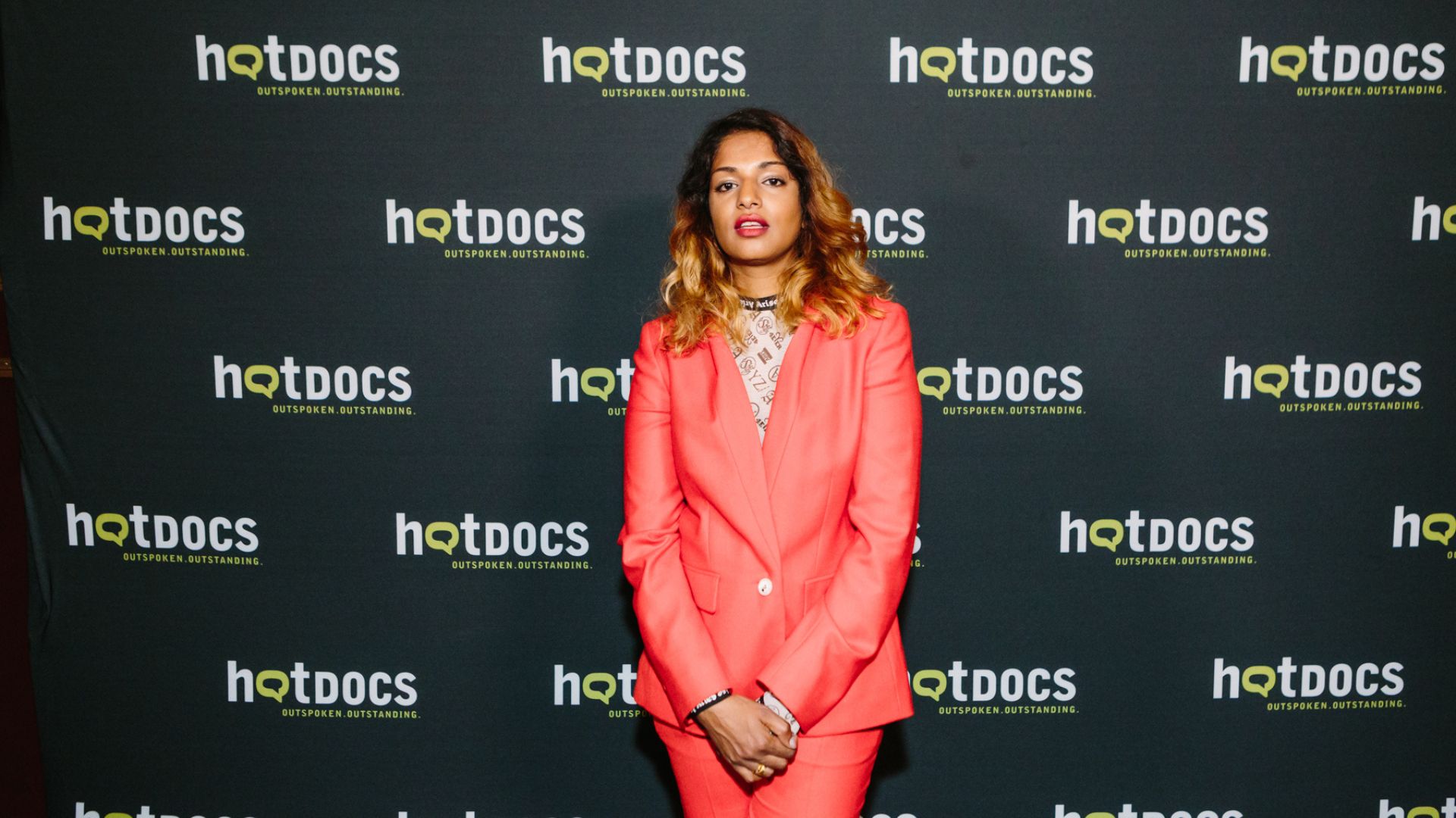 Music artist M.I.A. stands in front of a Hot Docs logo backdrop.